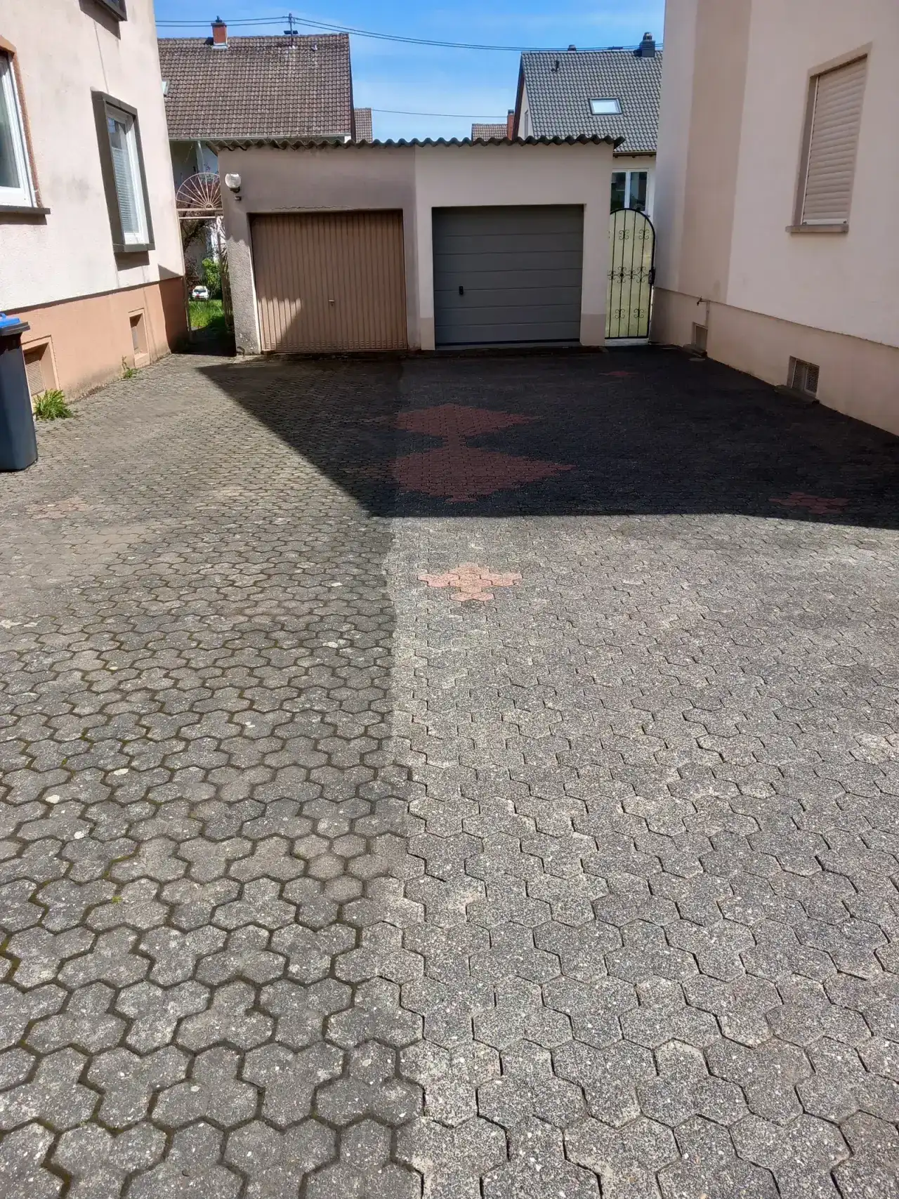 Hof aus Sechseckpflaster vor zwei Wohnhäusern mit Garagentor, die vordere Hälfte ist nass und hell, die hintere dunkel und trocken