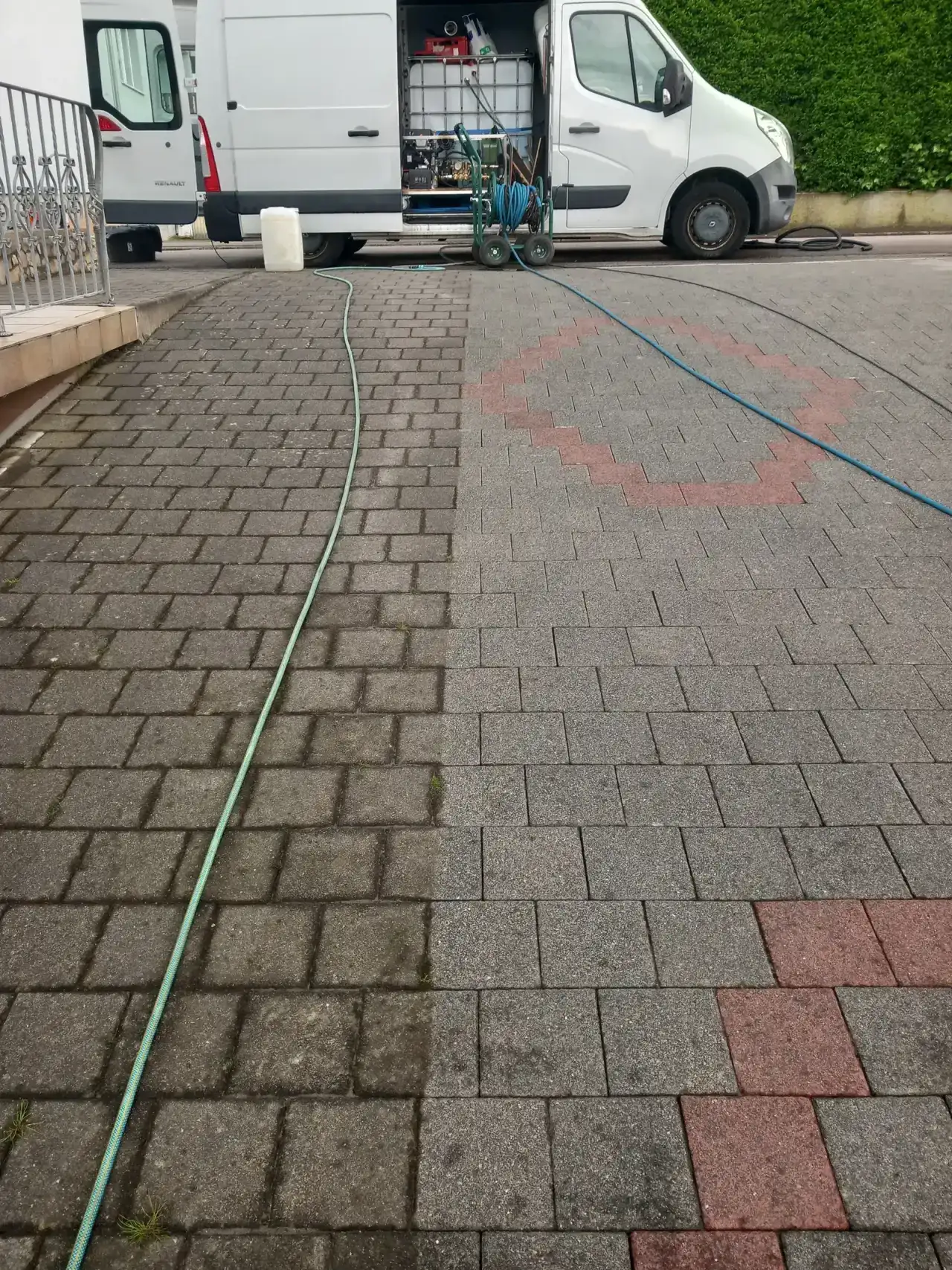 Einfahrt aus Betonpflaster mit einer schrägen Grenze zwischen dunkel bewachsenem und hellem Belag, ein Schlauch liegt quer, im Hintergrund ein weißer Transporter mit Ausrüstung