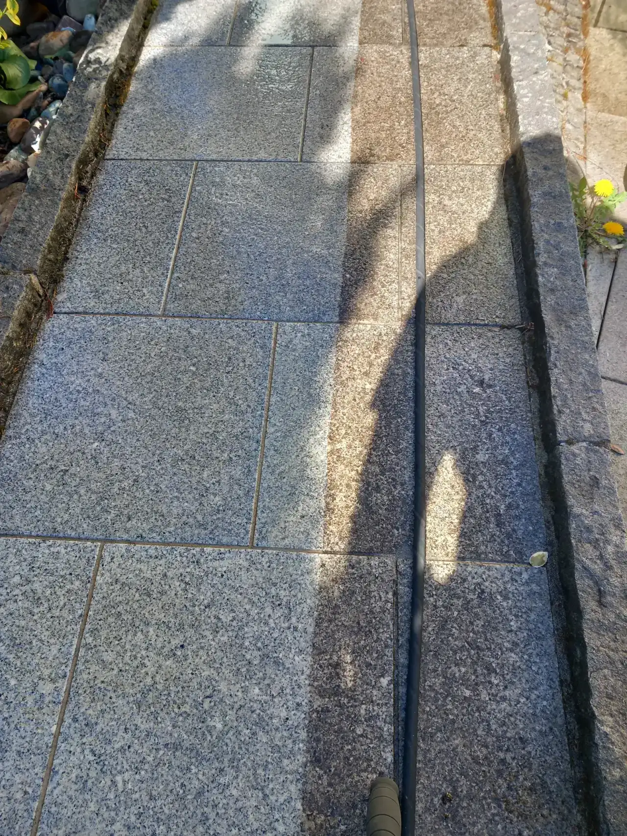 Weg aus hellen Granitplatten mit einer einzelnen Stufe, teils in hartem Schatten, der Belag ist gleichmäßig hell