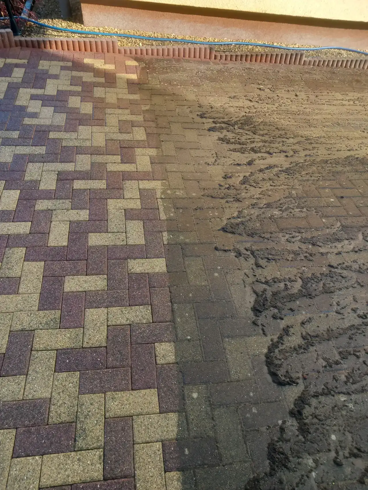 Betonpflaster in Gelb, Rot und Anthrazit, die linke Hälfte zeigt klare Steinfarben, auf der rechten liegt grauer Schmutzschlamm mit Schleifspuren