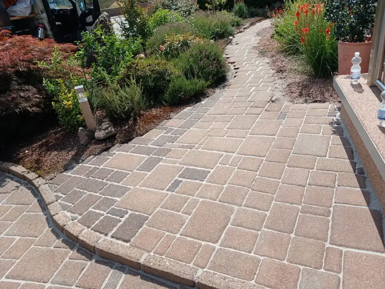 Nachher: Geschwungener Gartenweg aus Mehrformatpflaster mit dunklem Randstein zwischen zwei Pflanzbeeten, die Steinfarben sind klar und die Fugen hell gefüllt