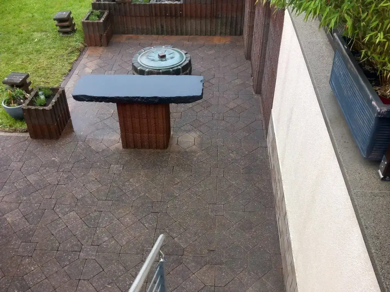 Gereinigte Gartenterrasse aus Betonpflaster mit Brunnen und Steinbank